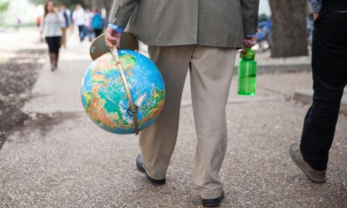 Person walking on sidewalk carrying a globe.