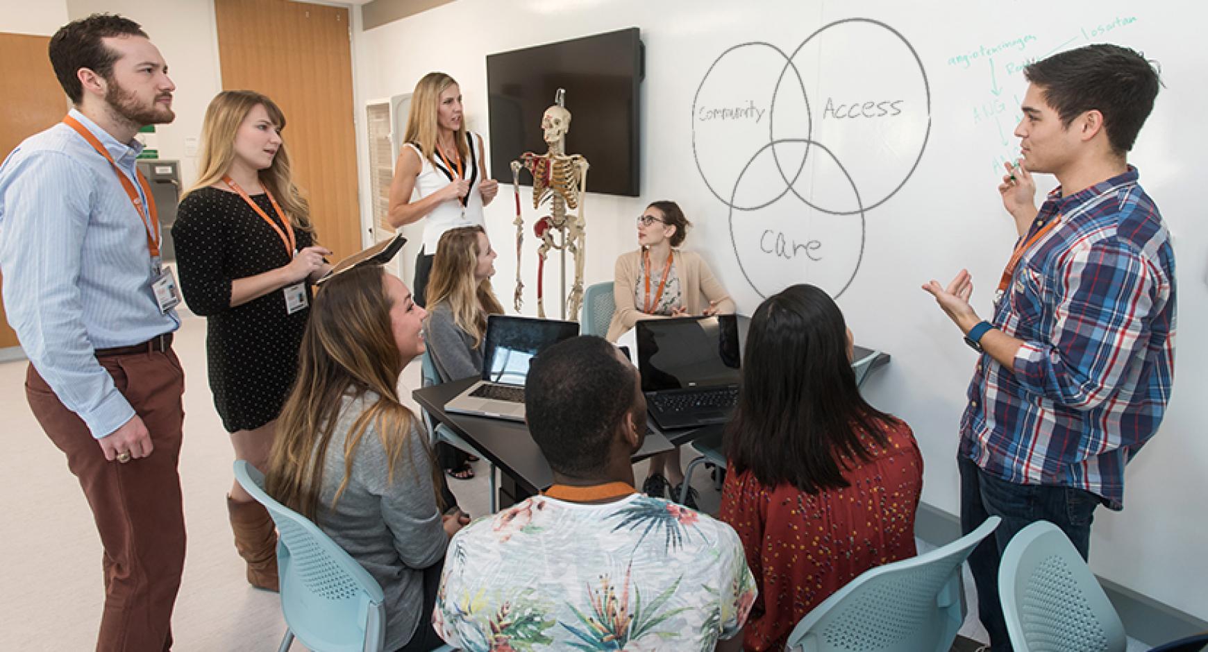 Students at the Dell Medical School working together at a desk next to a whiteboard