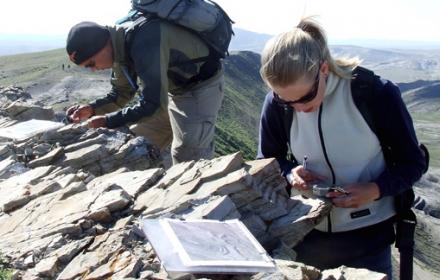 Students atop mountain on field trip examine rocks.