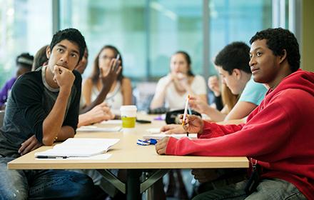 Undergraduate students sitting at table and listening to speaker.