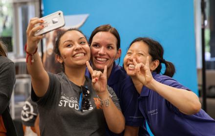 Student taking a photo while doing hook' em sign.